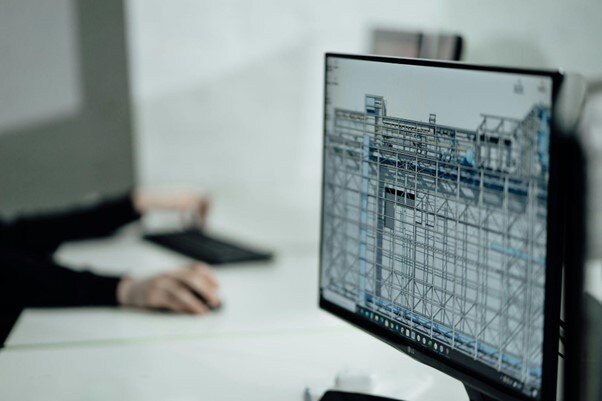 A person working at a computer with a detailed construction blueprint displayed on the screen, focusing on a complex building structure.}