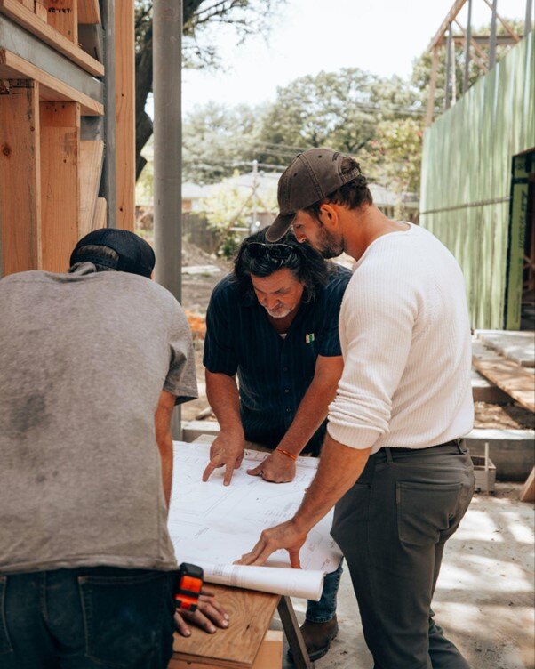 Three construction workers discussing blueprints on a building site