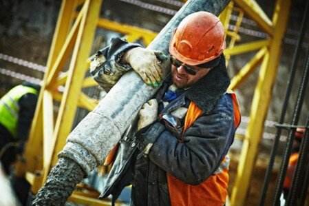 Worker in hard hat carrying concrete hose on construction site